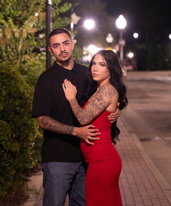 Couple posing together on a lamplit downtown sidewalk at night