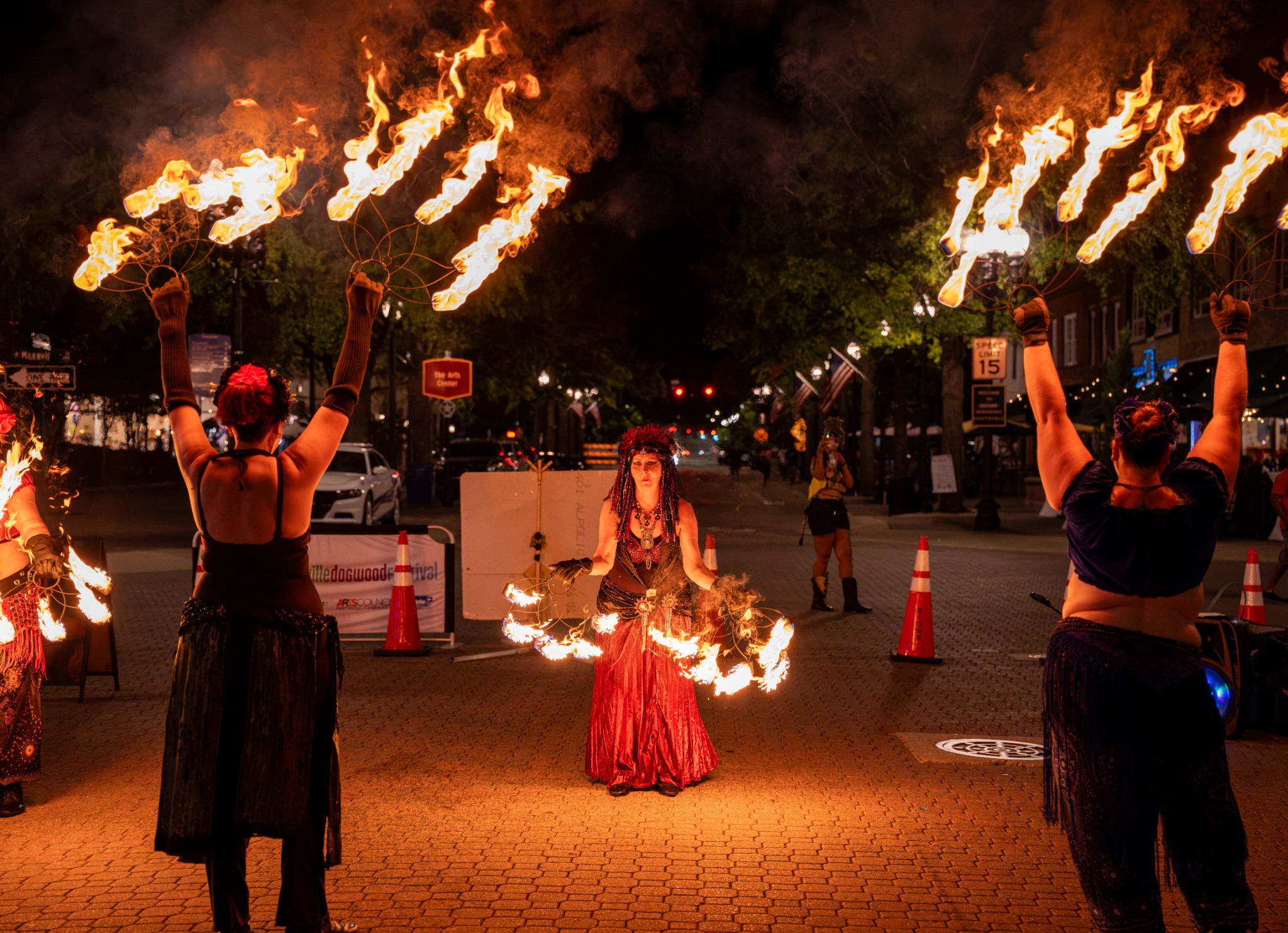 Fire performers raising flaming fans around a performer in a red skirt at Dogwood Nights