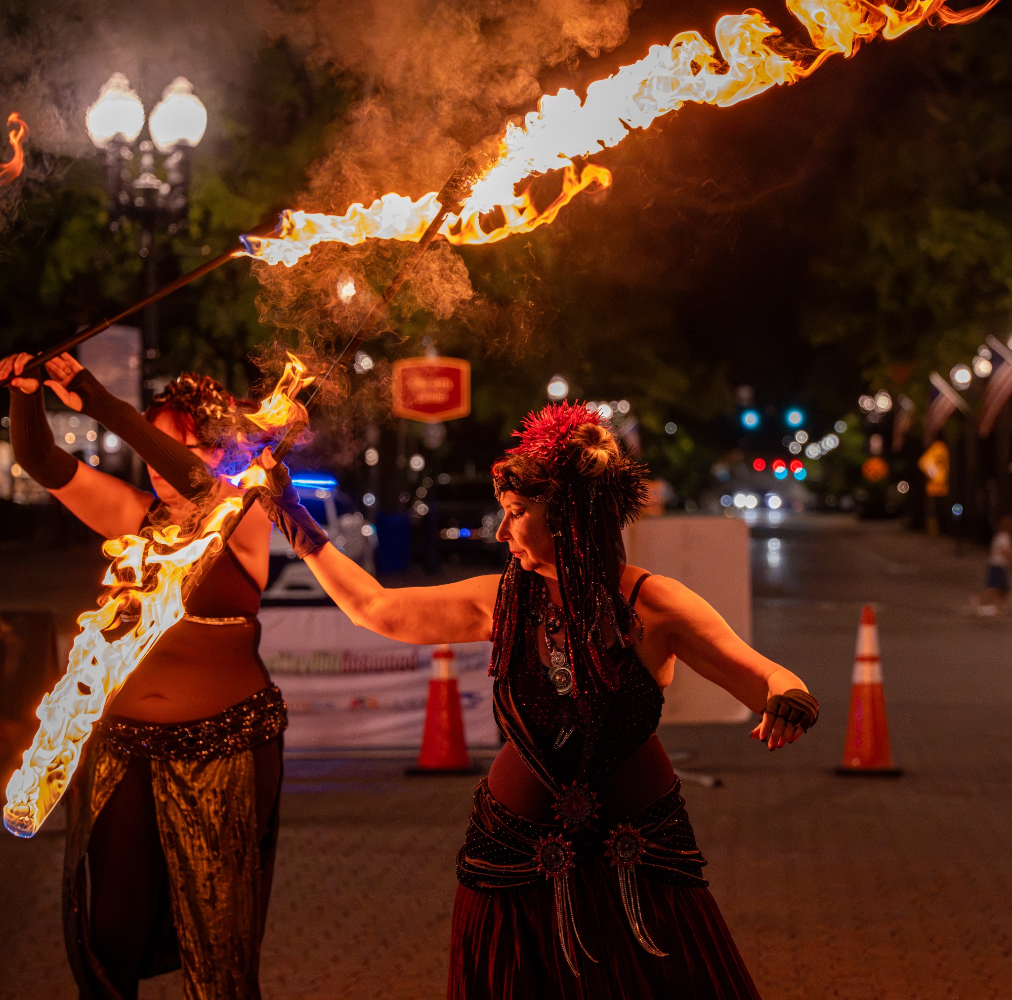 Two performers lifting flaming staffs during a nighttime street performance at Dogwood Nights