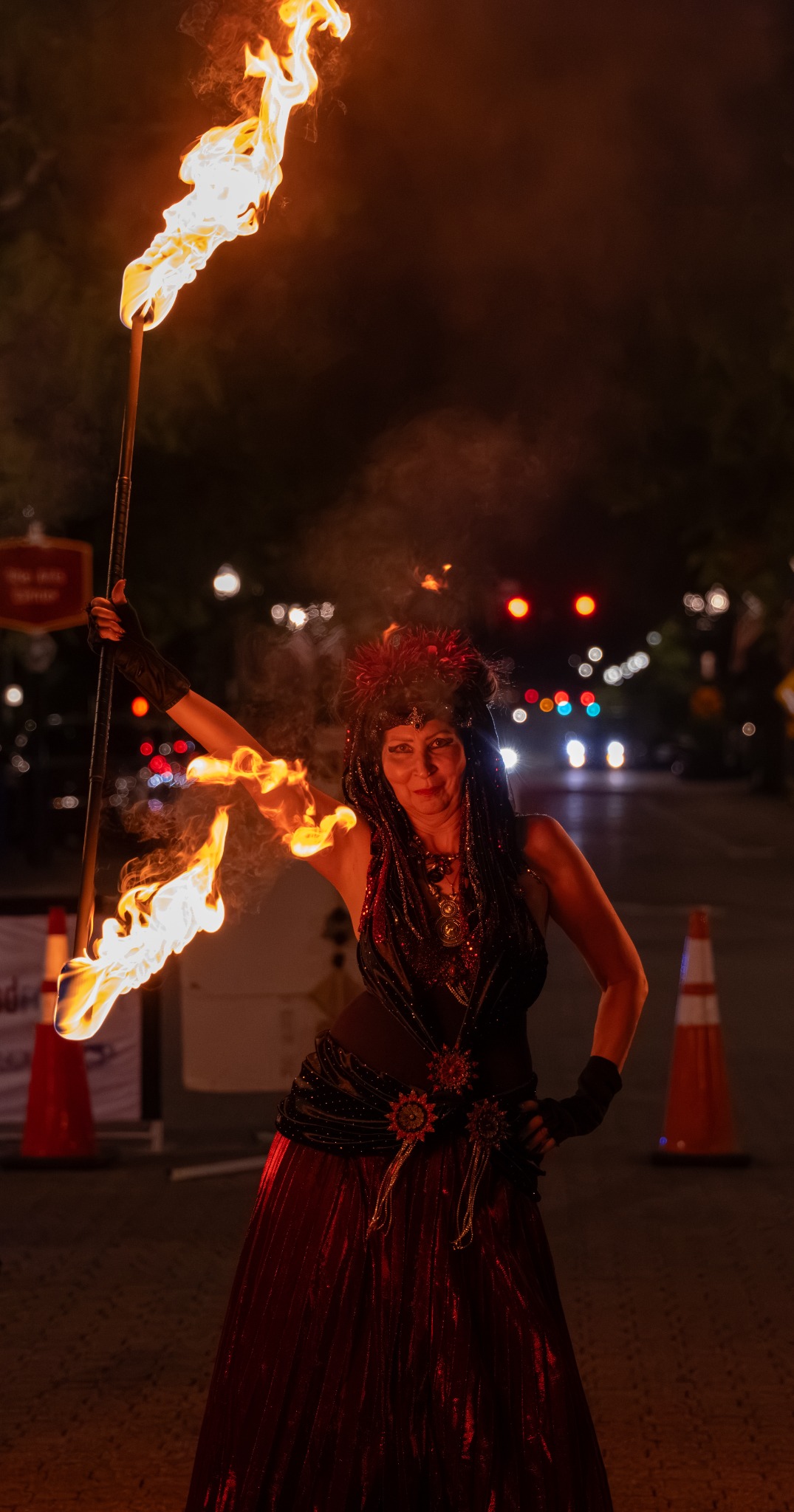 Fire performer in a red skirt holding a flaming staff upright at Dogwood Nights