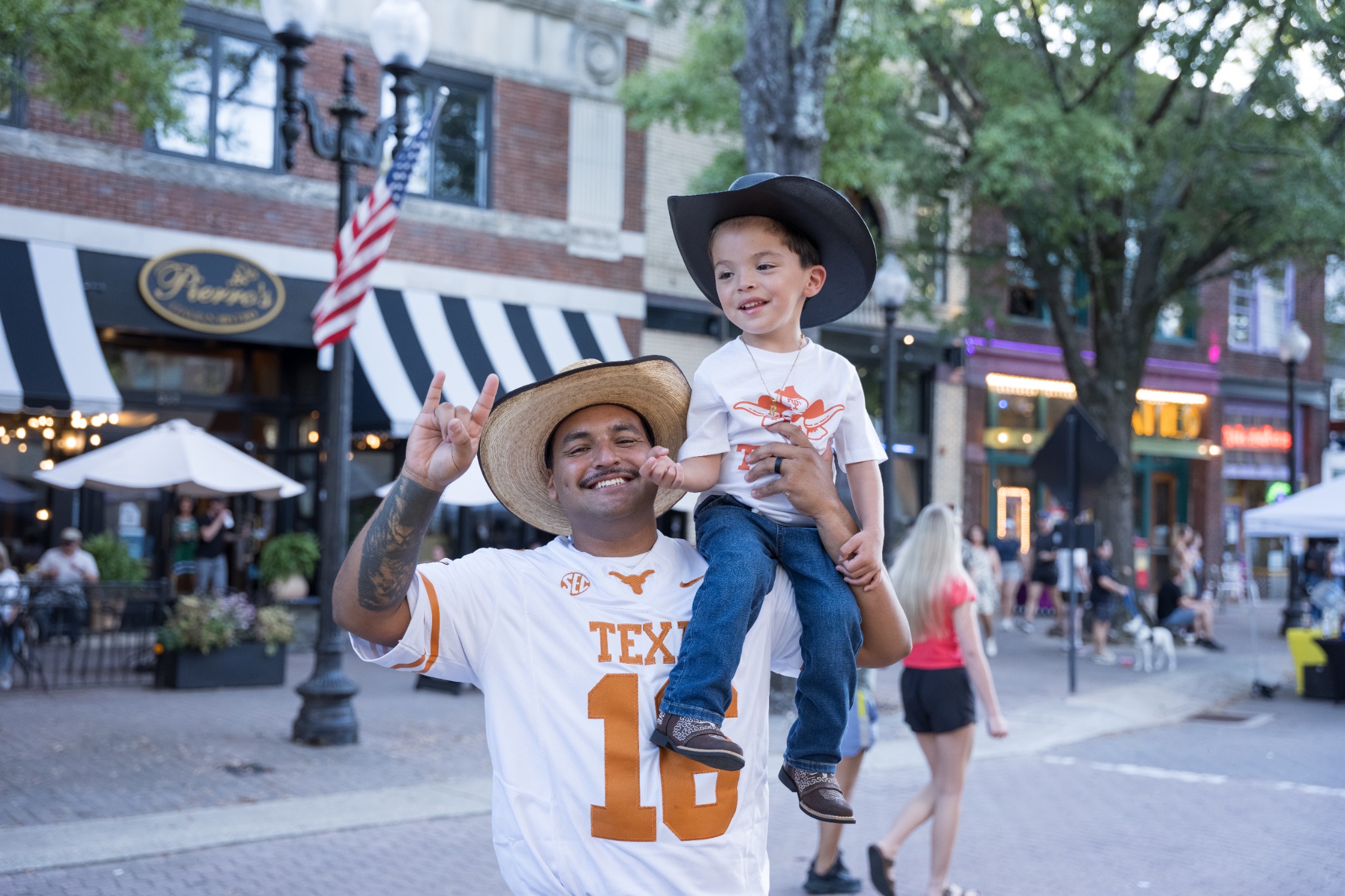 Smiling event guest in a white Texas jersey holding a child in a black cowboy hat