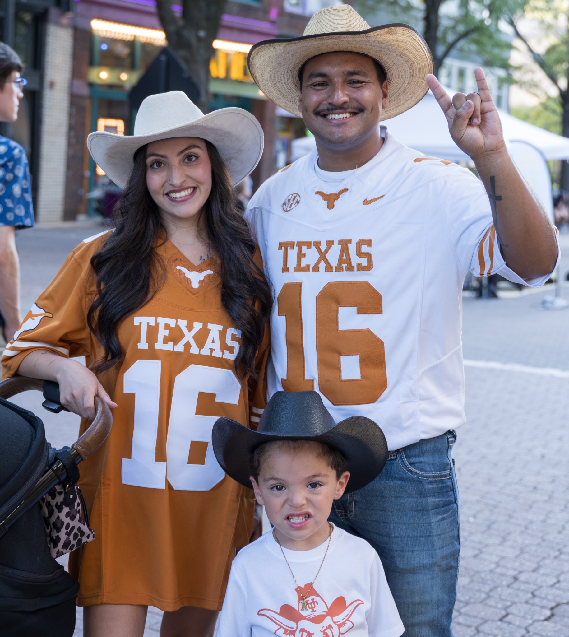 Two event guests in Texas jerseys and cowboy hats posing with a child in a black cowboy hat