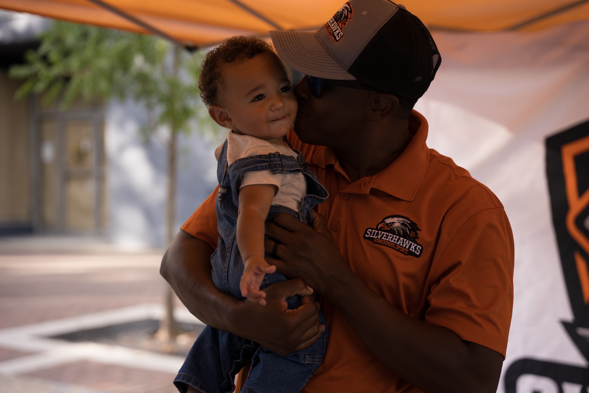 Event guest kissing a baby on the cheek beneath an orange canopy