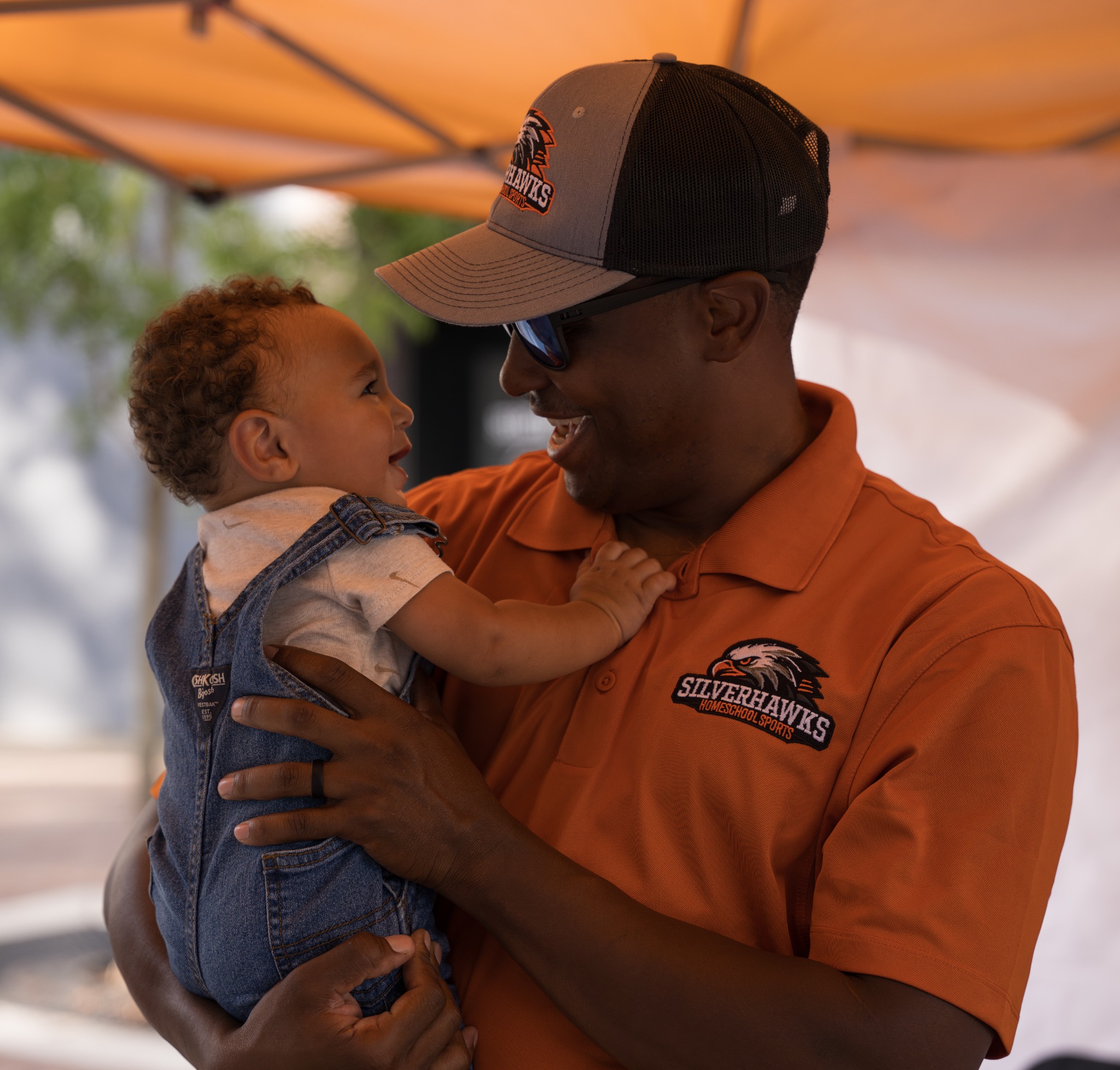 Event guest and baby smiling at one another beneath an orange canopy