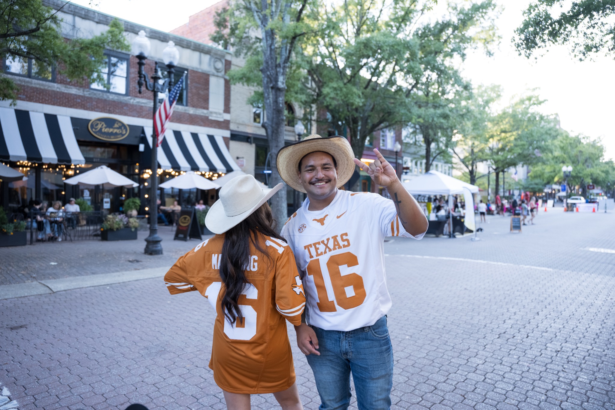 Two event guests in matching Texas jerseys and cowboy hats sharing a moment on the street